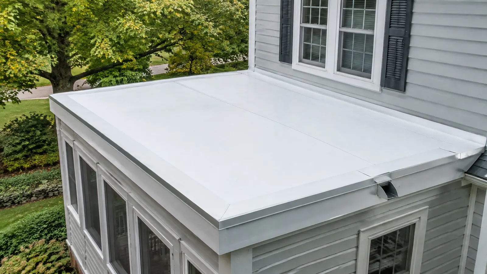 New white membrane roof over a one-story rear addition, with edge metal and a scupper, beside a two-story clapboard wall